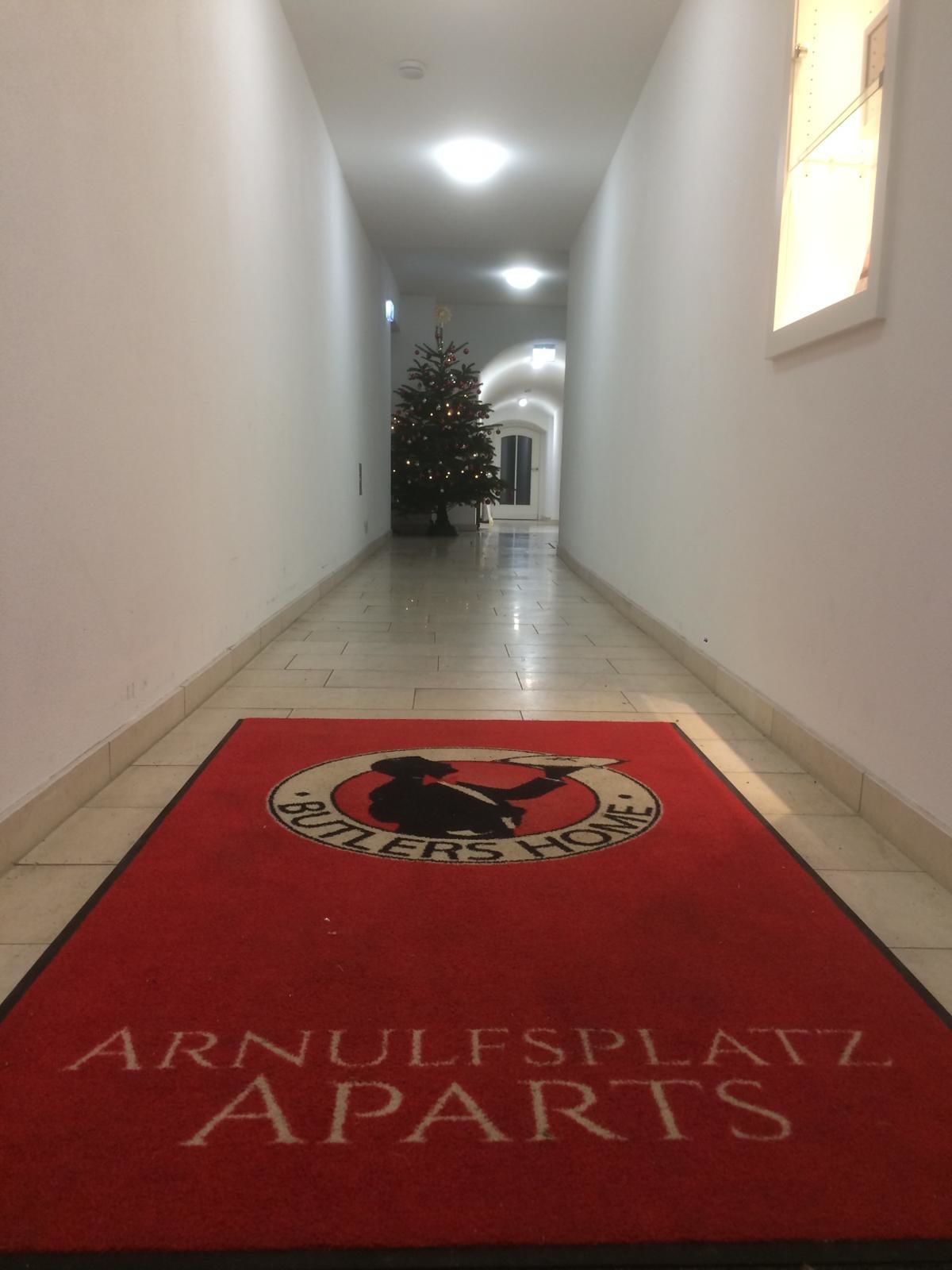 A hallway with a red carpet leading to a Christmas tree and a door.