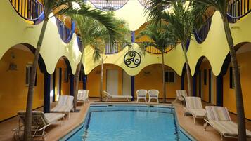 An indoor swimming pool with lounge chairs and palm trees, surrounded by yellow walls and blue railings.