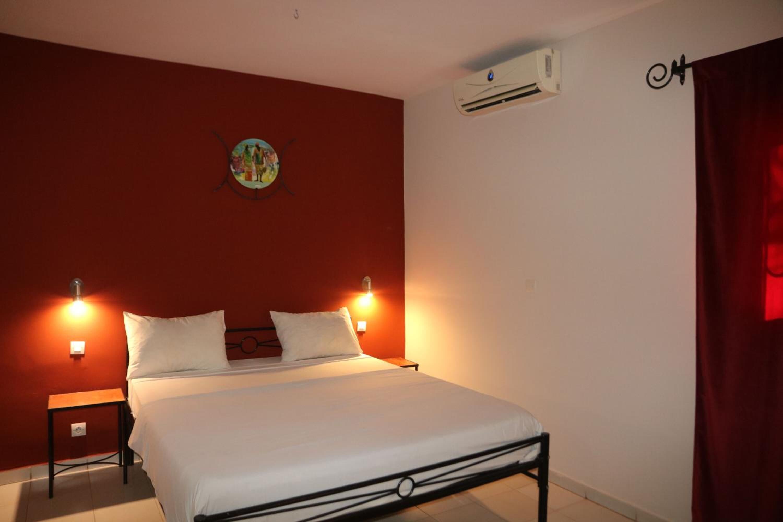 A single bed with white bedding, two bedside tables, a wall-mounted air conditioner, and a red curtain.