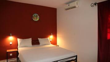 A single bed with white bedding, two bedside tables, a wall-mounted air conditioner, and a red curtain.