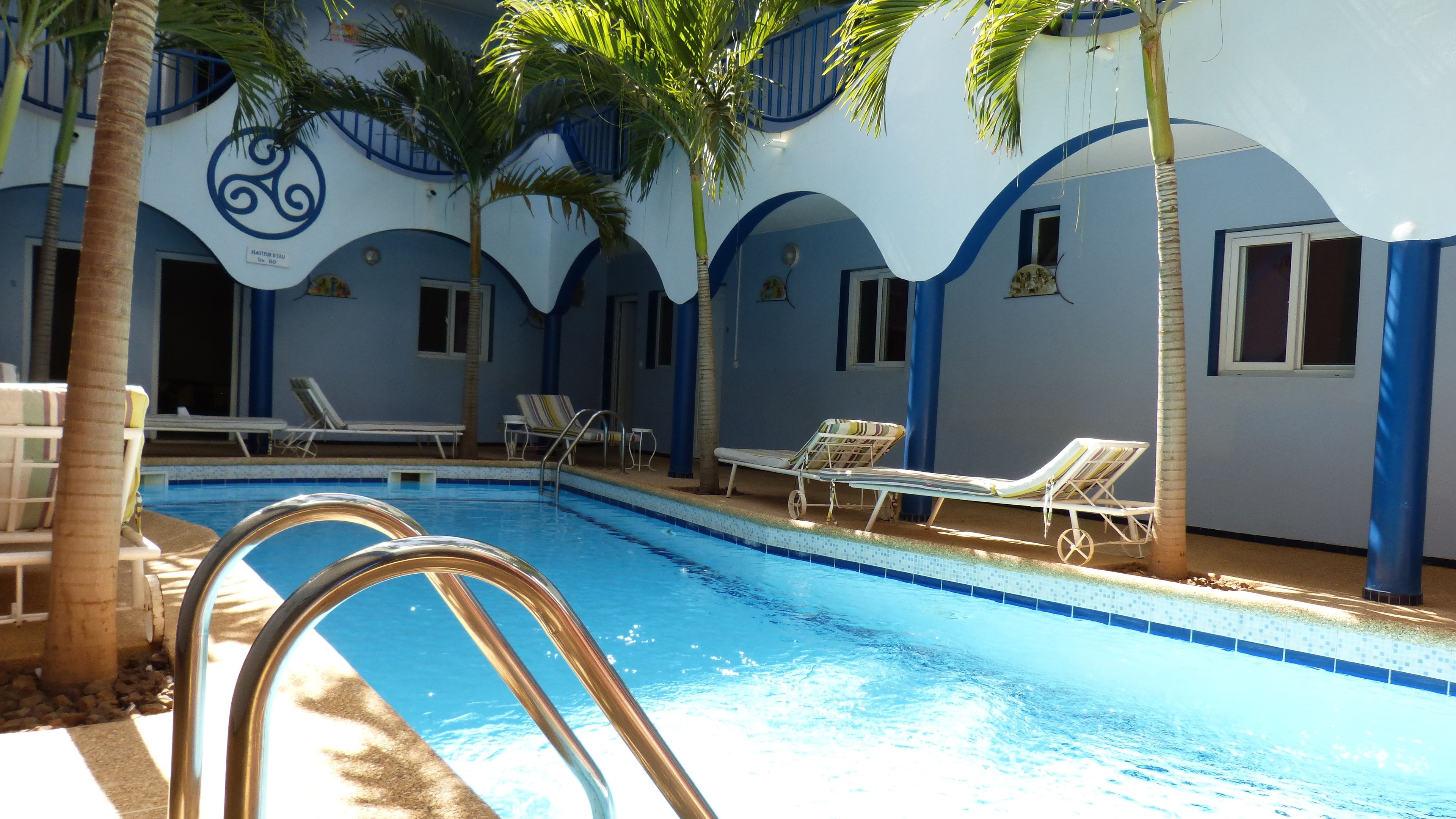 Un área de piscina con sillones de descanso y palmeras.