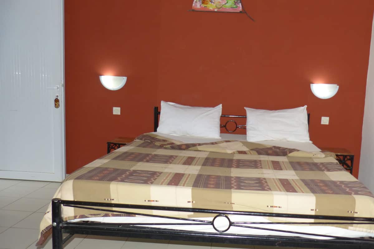 A single bed with a patterned bedspread, two white pillows, and two bedside tables with wall-mounted lamps.
