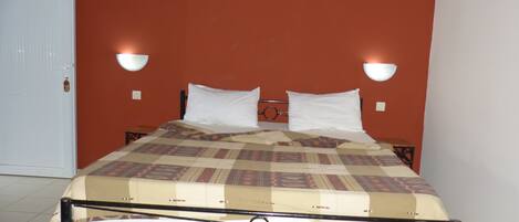 A single bed with a patterned bedspread, two white pillows, and two bedside tables with wall-mounted lamps.