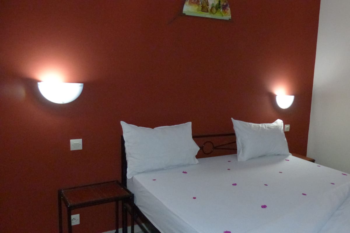 A hotel room with a bed, two white pillows, a small bedside table, and two wall-mounted lights.