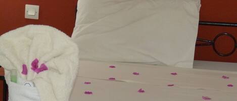 A bed with a white pillow and a white blanket with purple flower patterns.
