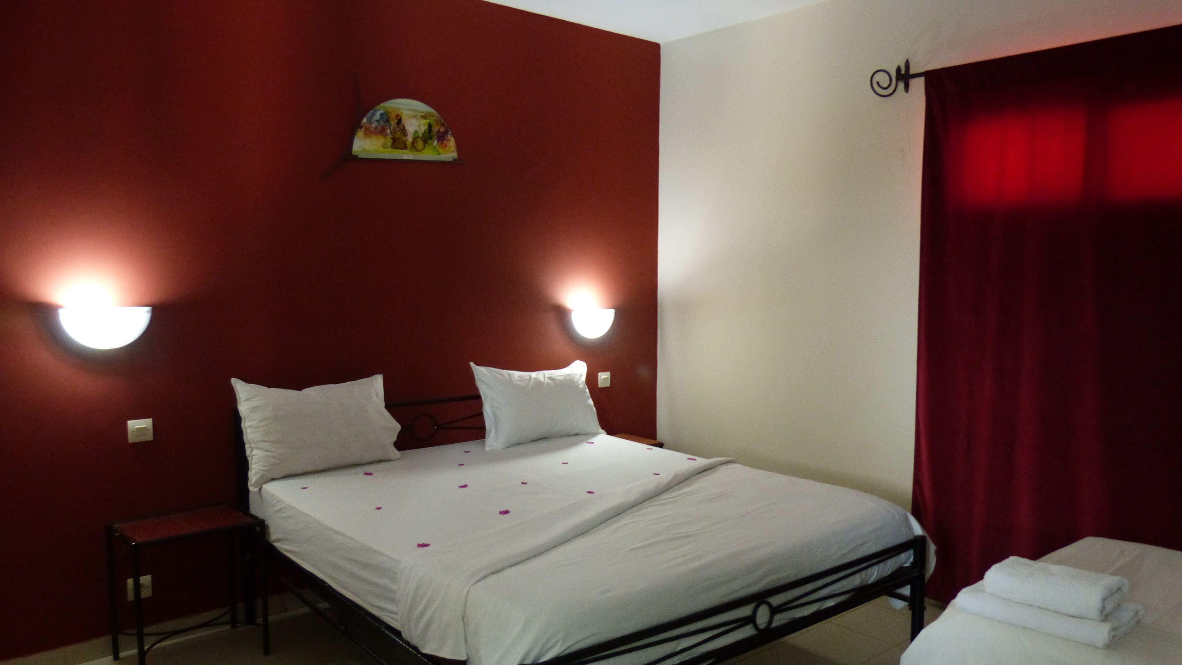 A hotel room with a bed, two bedside lamps, a small table, and a red curtain.