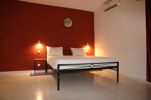 Un dormitorio con una cama, dos mesitas de noche, un aire acondicionado de pared y un reloj de pared.