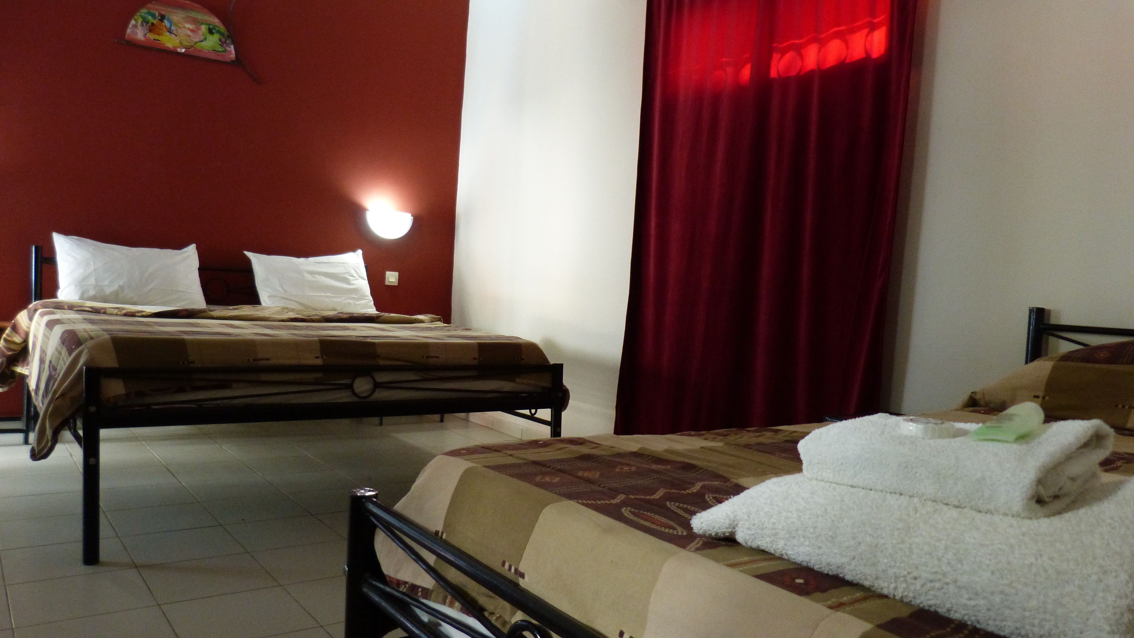 Una habitación con dos camas, una con cortina roja y otra con cortina blanca.