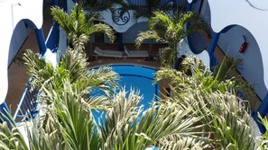 Una piscina rodeada de palmeras, sillas de descanso y un edificio azul y blanco con un letrero.