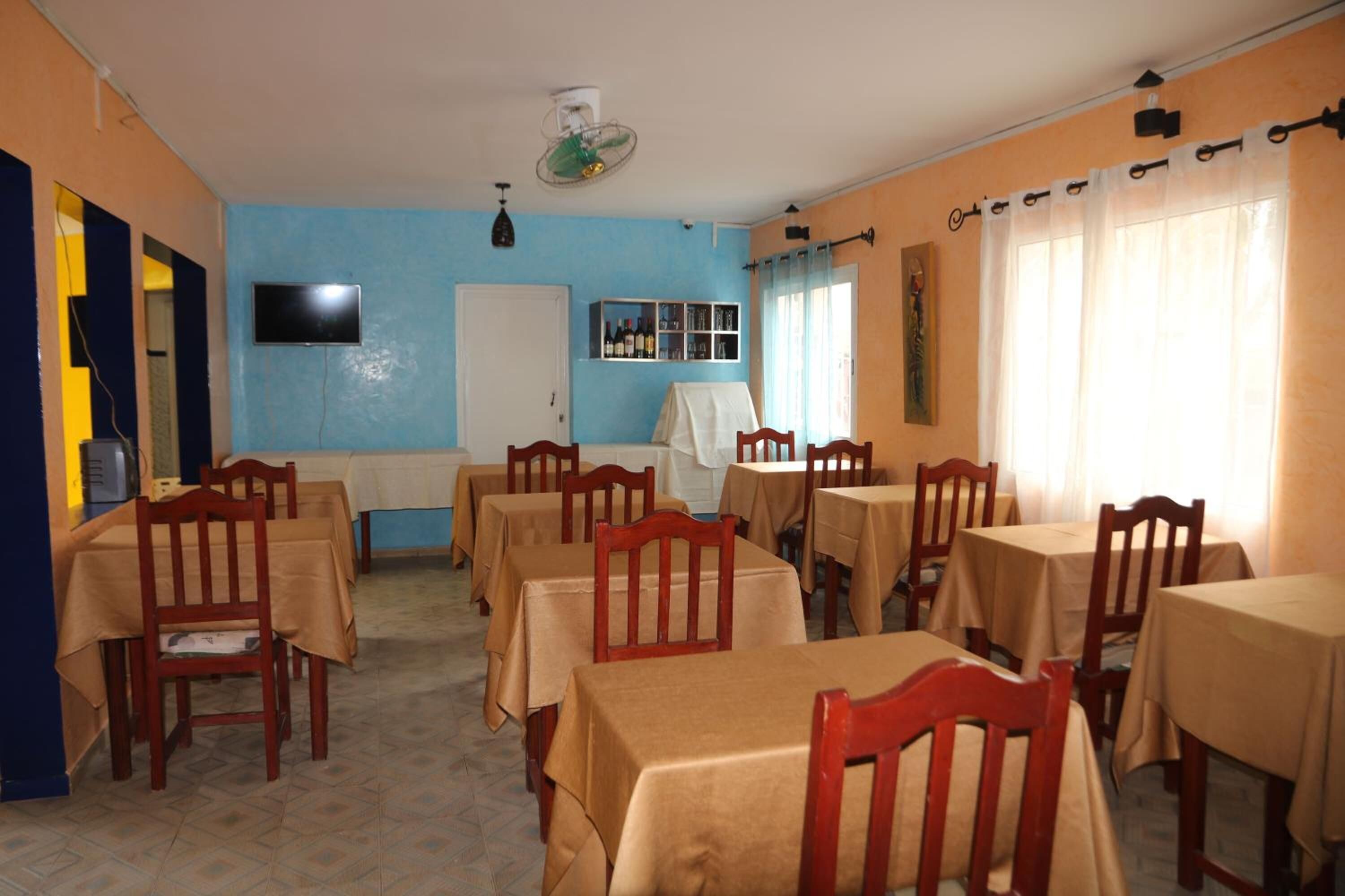 Un comedor con varias mesas y sillas, un televisor montado en la pared y un ventilador de techo.