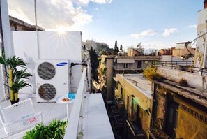 A rooftop terrace with an air conditioning unit, a white chair, and a small table with snacks.