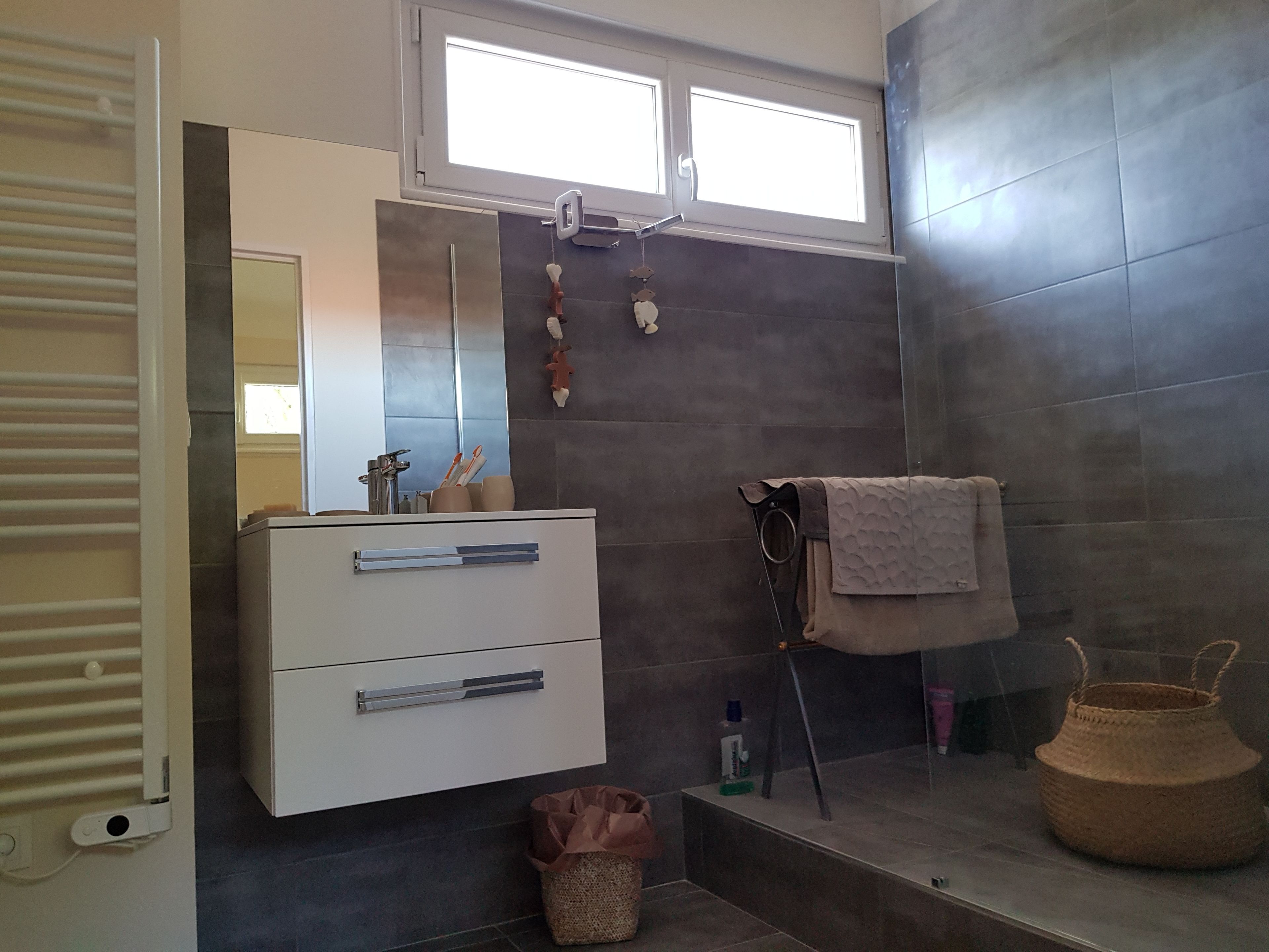 A modern bathroom with a white vanity, a mirror, a towel rack, and a shower area.