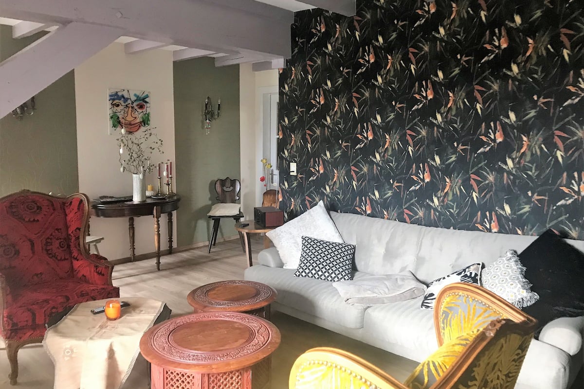 Una sala de estar con sofá blanco, sillón estampado y un adorno de pared.