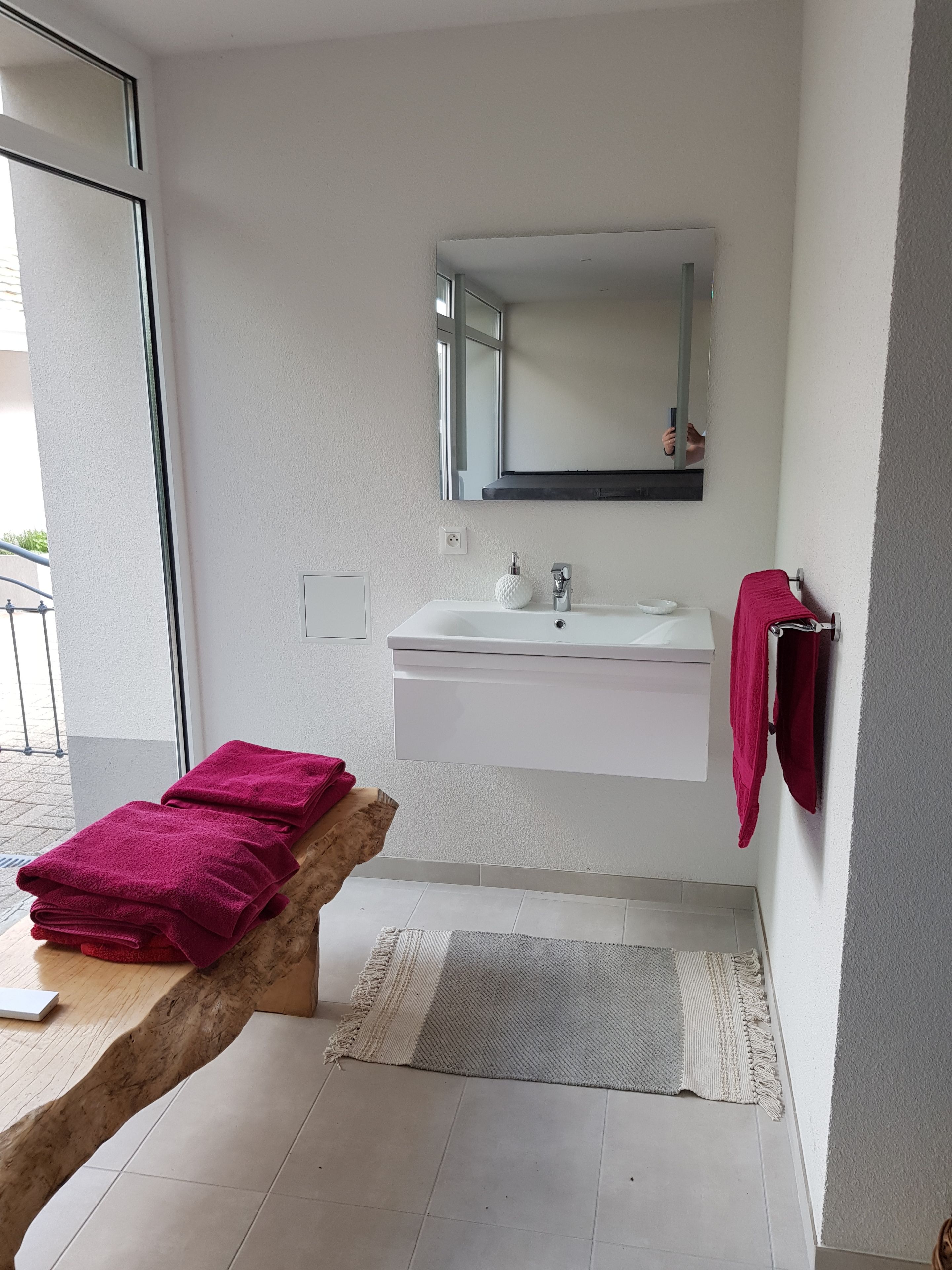 A modern bathroom with a white sink, a mirror above it, and a wooden bench with towels.