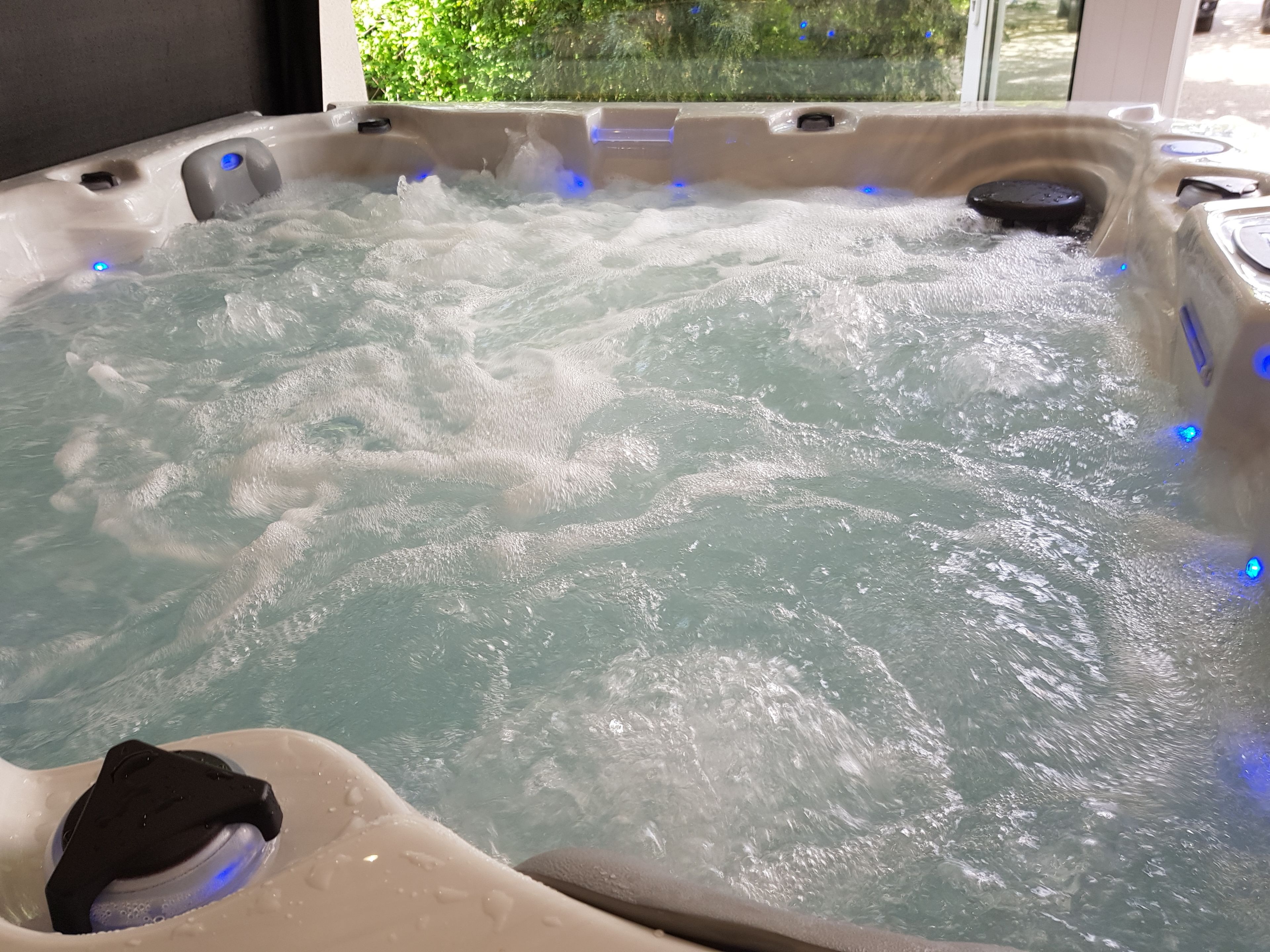 A hot tub with visible bubbles and a black object inside, surrounded by a beige tub with blue lights.