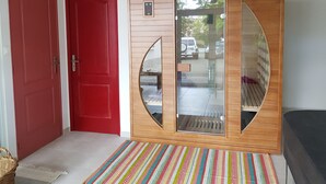 A room with a red door, a wooden wardrobe with a glass panel, and a colorful striped rug. - La Roseraie (Sentheim)