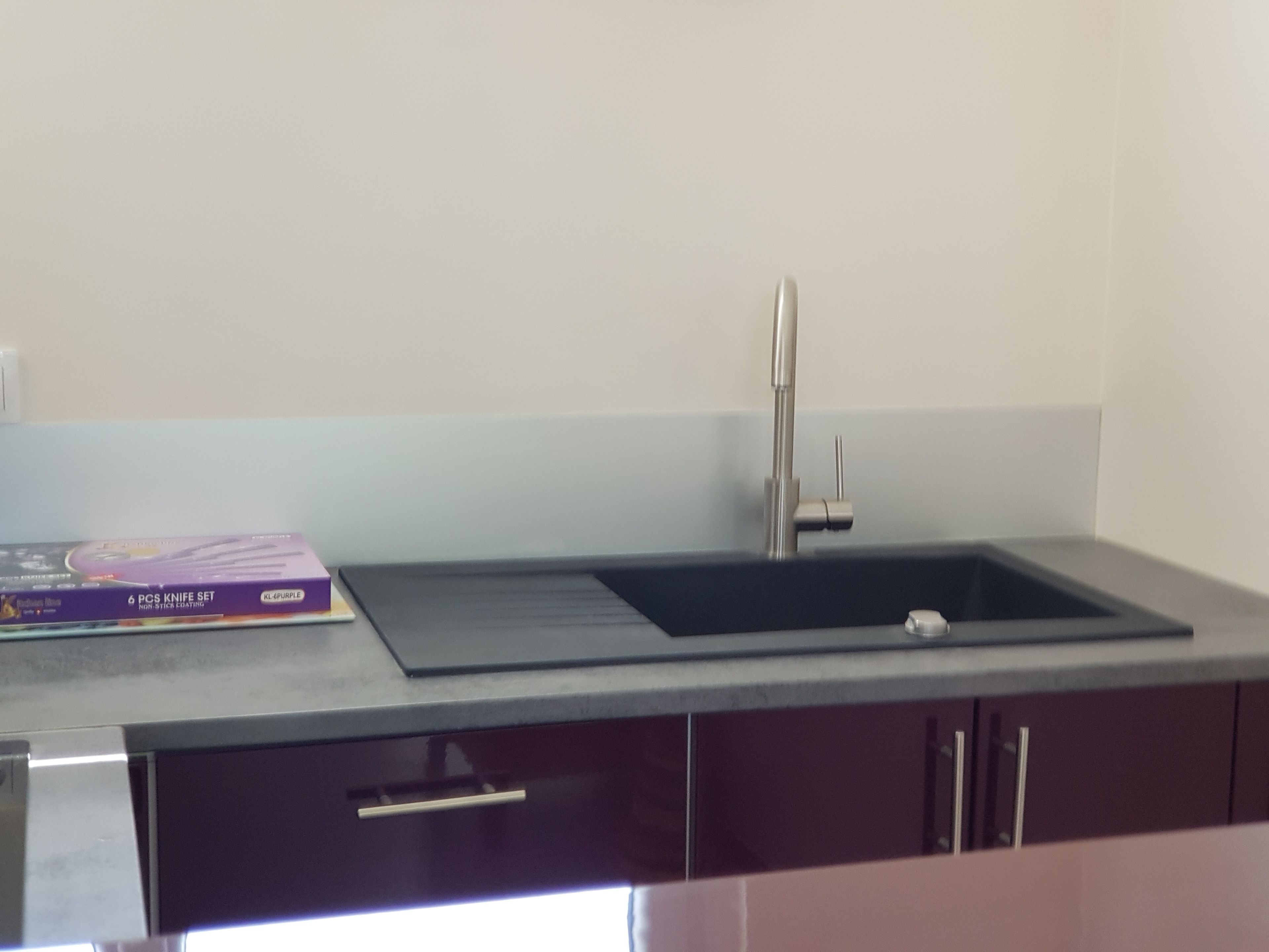 Una cocina con encimera negra, un lavamanos de acero inoxidable y una caja morada sobre la encimera.