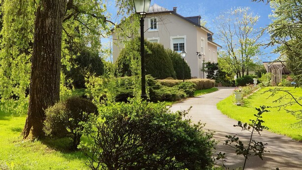 A house with a paved driveway, surrounded by lush greenery and a well-maintained garden. - La Roseraie (Sentheim)