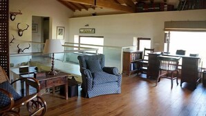 A spacious living area with a high ceiling, wooden beams, a staircase, and a view of the outdoors.