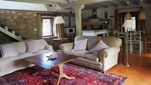 A spacious living room with a high ceiling, a stone wall, a sofa, a coffee table, and a patterned rug.