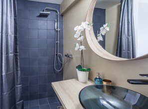 A modern bathroom with a shower, a sink with a glass basin, a mirror, and a potted orchid.