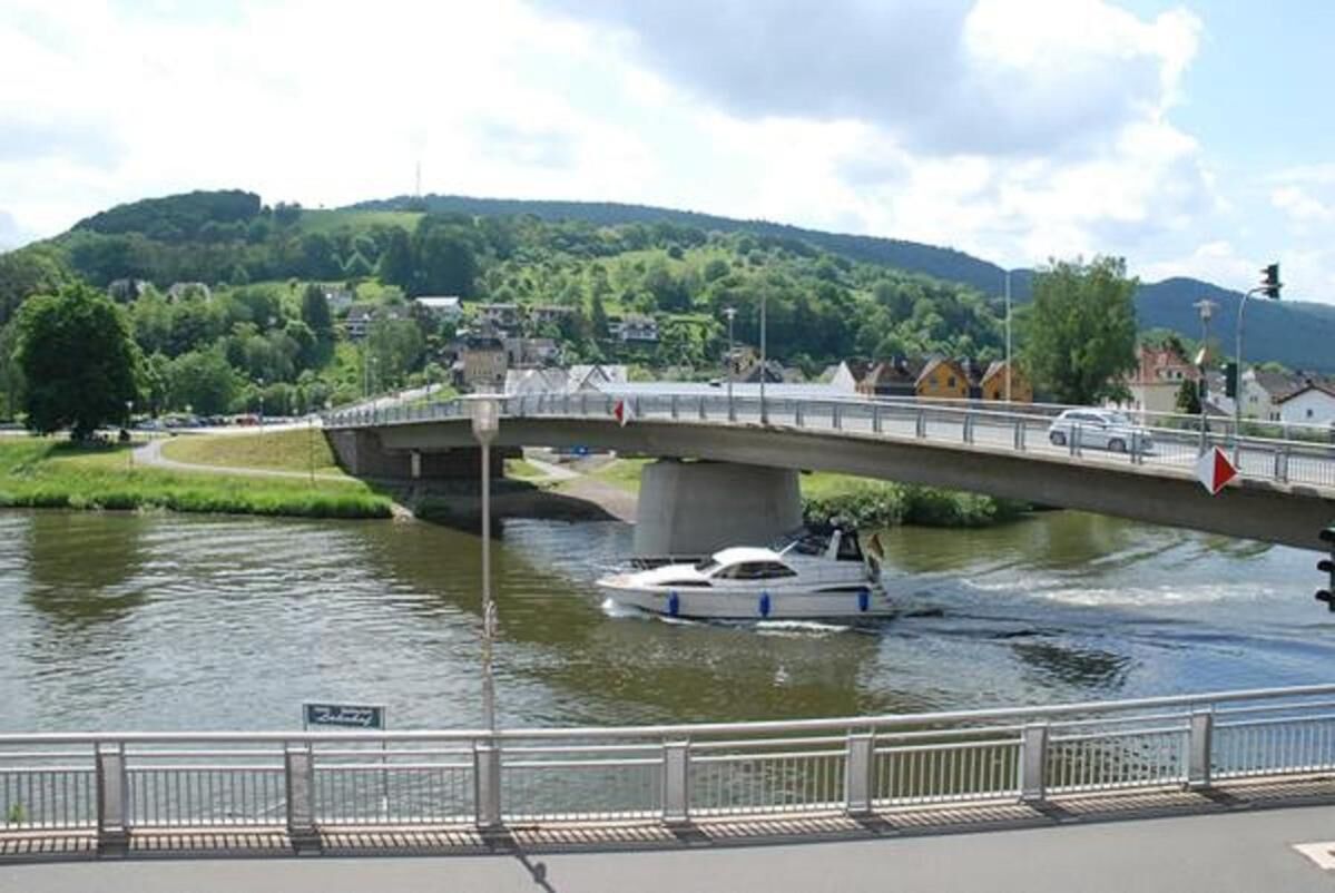 A bridge over a river with a boat, surrounded by greenery and buildings.