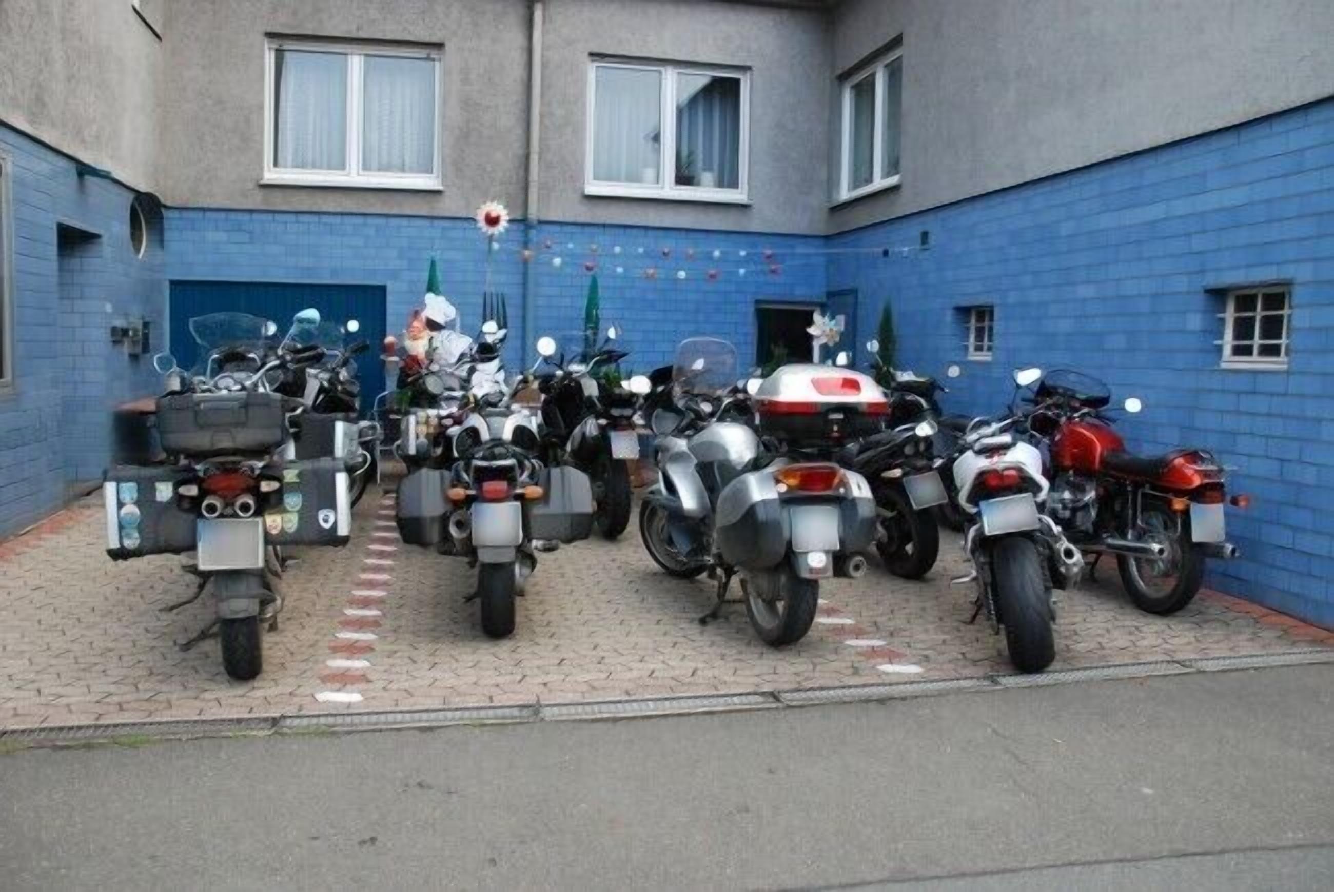 Un patio con varias motocicletas estacionadas frente a un edificio de paredes azules y ventanas blancas.