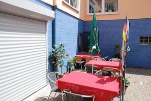 Une terrasse extérieure avec des tables et des chaises, une porte de garage fermée et un mur bleu.