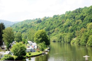 Un terrain de camping au bord de la rivière, avec des emplacements pour camping-cars et des possibilités d’amarrer des bateaux, le tout entouré de collines verdoyantes.