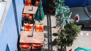 Une terrasse extérieure avec des tables et des chaises, une plante en pot et une voiture garée.