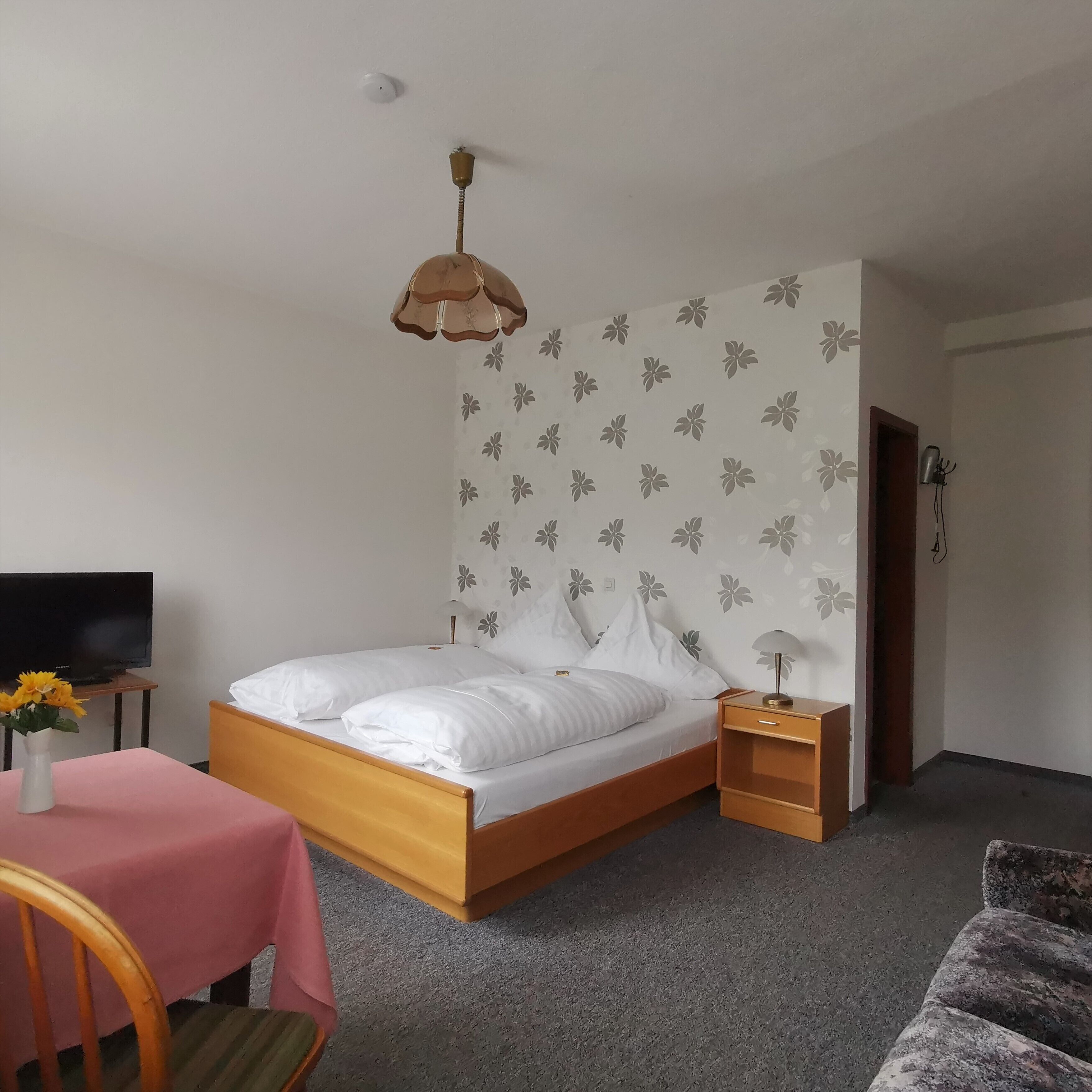A bedroom with a bed, bedside table, lamp, TV, and a chair with a table.