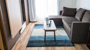 Un salon avec un canapé, une petite table sur laquelle est posée une plante, et une fenêtre avec des rideaux.