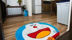 Une cuisine avec un plancher en bois, un réfrigérateur blanc, une poubelle bleue et un tapis aux motifs félins bleus et blancs.
