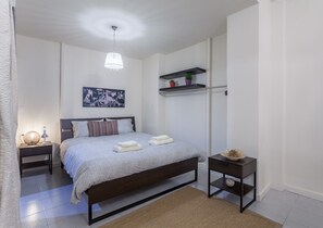 A modern bedroom with a bed, bedside tables, a hanging light fixture, a shelf with decorative items, and a painting on the wall. - A Gift in the Heart of Monastiraki B (Athens)
