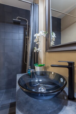 A modern bathroom with a glass bowl sink, a black faucet, a shower with a curtain, and a potted orchid. - A Gift in the Heart of Monastiraki B (Athens)