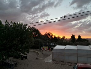 Un jardín con invernadero, mobiliario exterior y una puesta de sol al fondo.