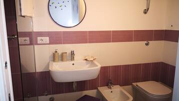 A bathroom with a sink, bidet, toilet, and a mirror with decorative elements.