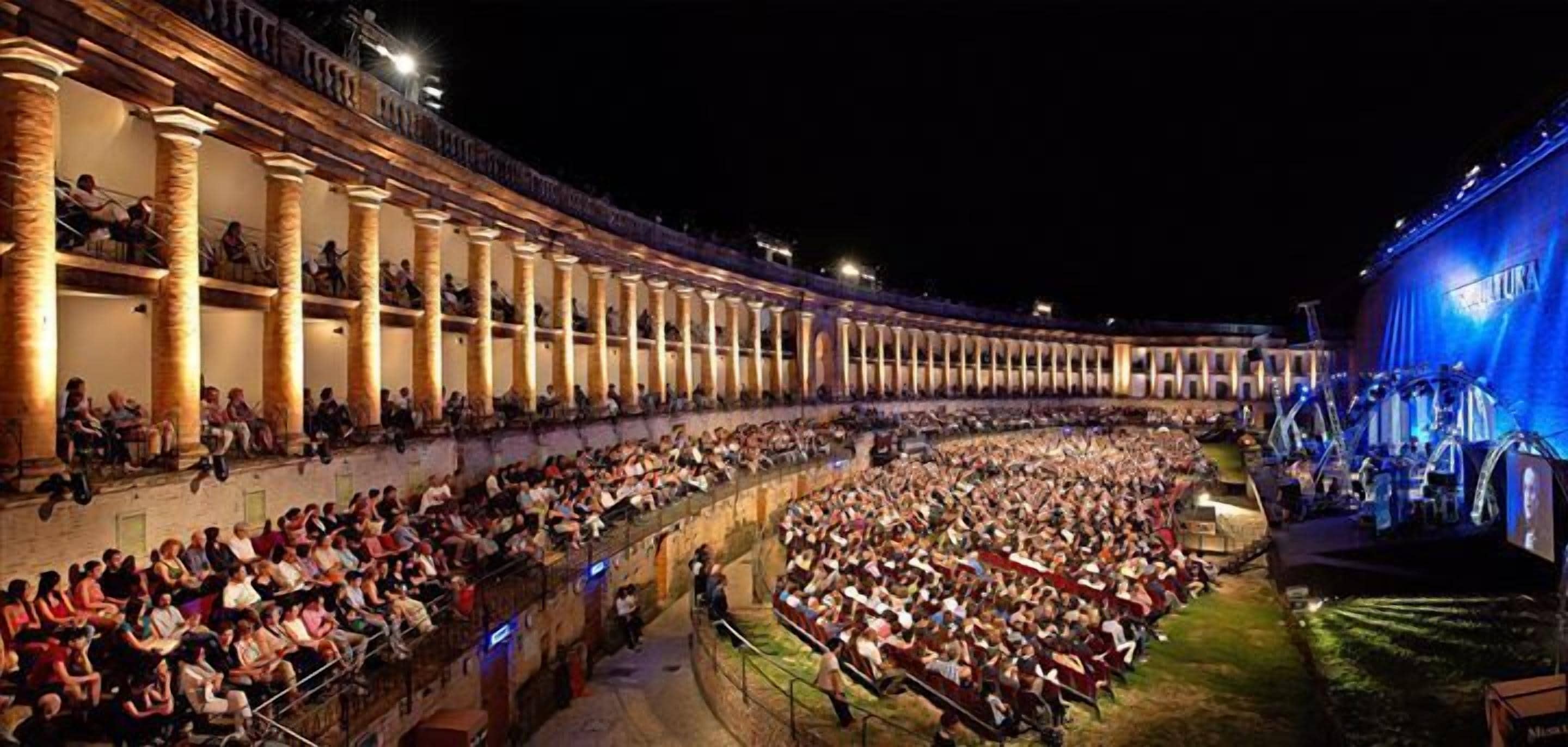 Um grande anfiteatro histórico com assentos em terraços e uma área de palco.