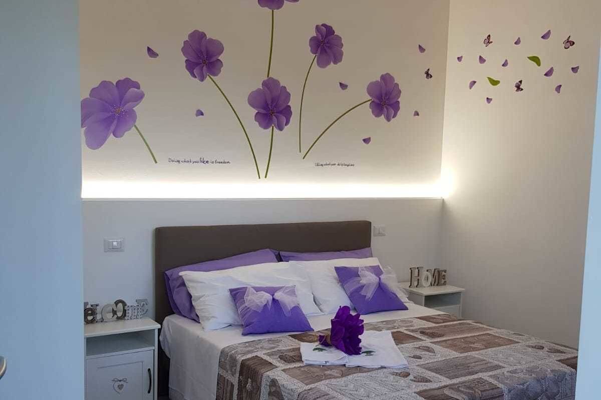 A bedroom with a bed, nightstands, and a wall decoration of purple flowers.