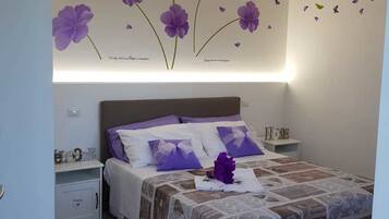 Ein Schlafzimmer mit Bett, Nachttischen und einer Wanddekoration mit violetten Blumen.