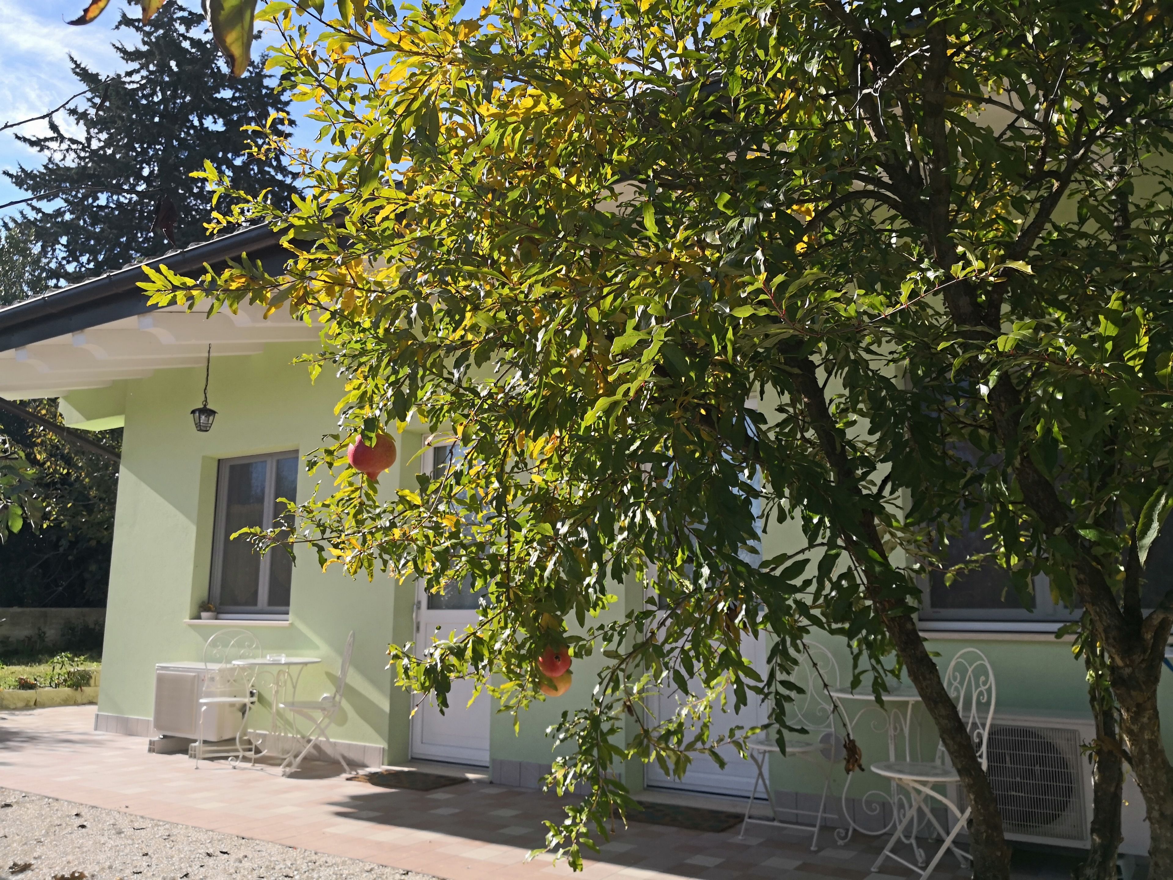 A small, single-story building with a green exterior, a window, and a door. There are outdoor chairs and a table near the entrance.