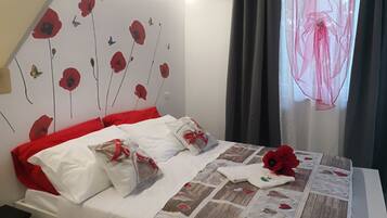 Una cama bien hecha con ropa de cama blanca y roja, un colcha con motivos florales y una pared decorada con flores y mariposas rojas.