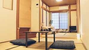 Habitació japonesa tradicional amb fons de tatami, una taula baixa, coixins i una porta corredissa que dona a una altra habitació.