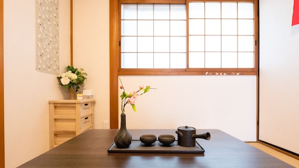 Una habitació japonesa tradicional amb sòls de tatami, una taula de fusta baixa, un jeu de te, un ram de flors i un panell shoji al fons de la taula.
