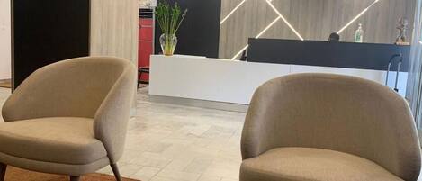 Un área de recepción con dos sillones, un mostrador y una planta decorativa.