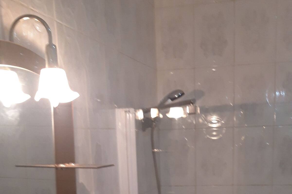 A bathroom with a glass shelf, a sink, a mirror, and a shower area.