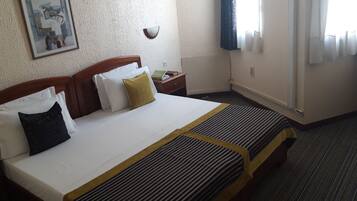 Una habitación de hotel con una cama, una mesita de noche, una lámpara y una ventana con cortinas.