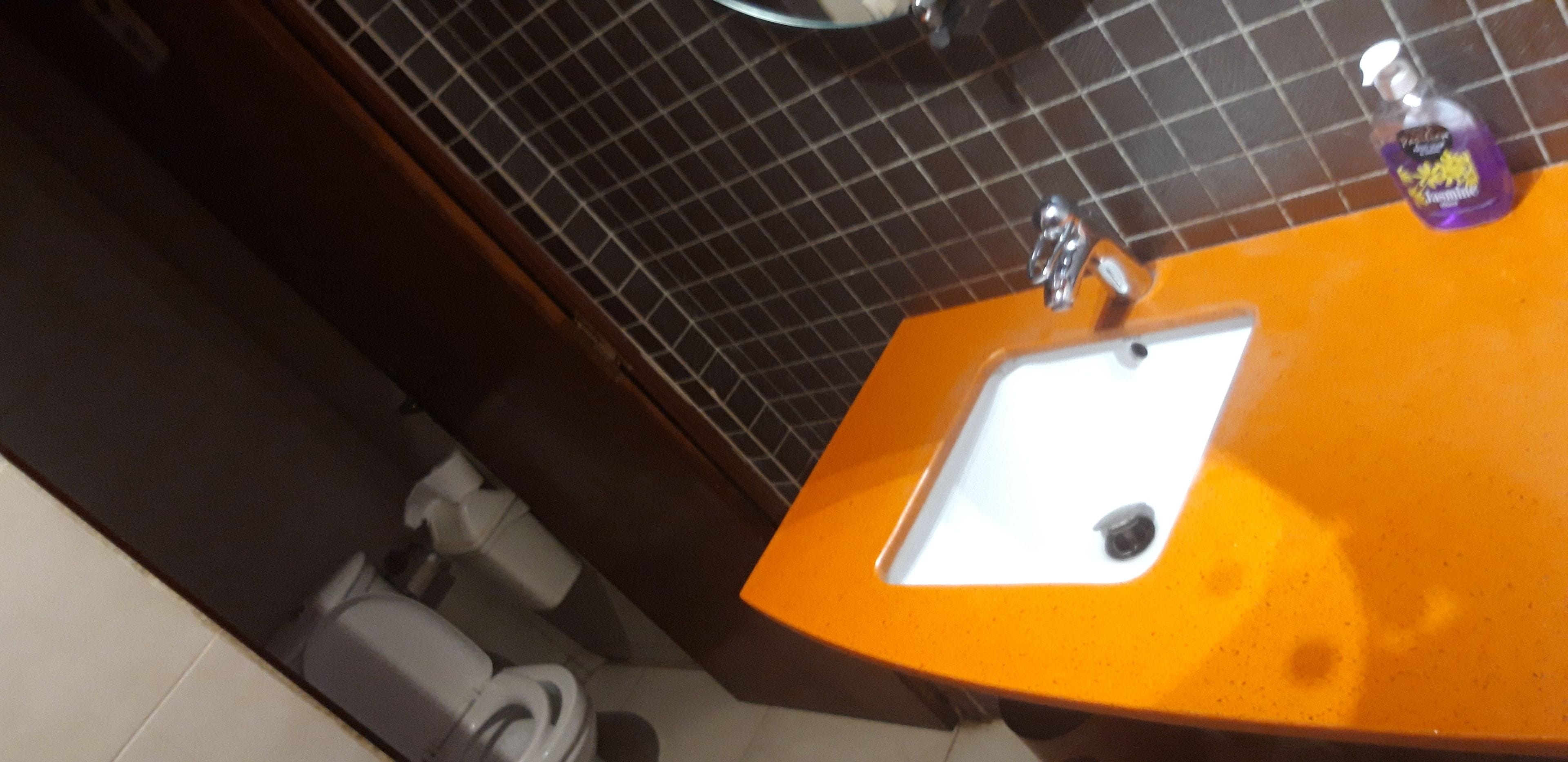 A bathroom with a white sink, an orange countertop, and a black tiled wall.