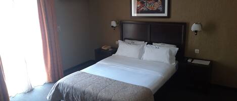 A hotel room with a large bed, a nightstand with a telephone, and a wall-mounted lamp.