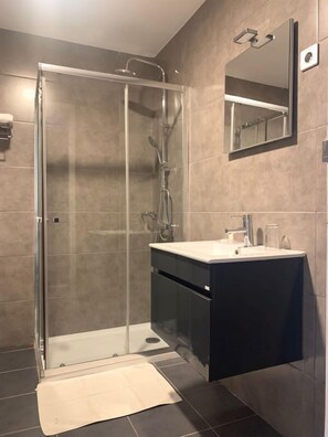Bathroom features a glass-enclosed shower, handheld showerhead, and wall-mounted faucet.